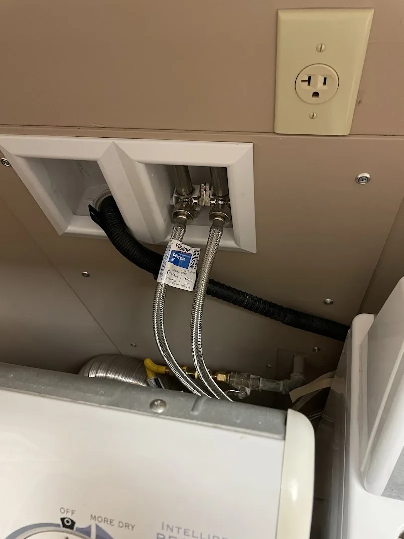 Laundry hookup showing braided supplies, drain hose, and a gas line